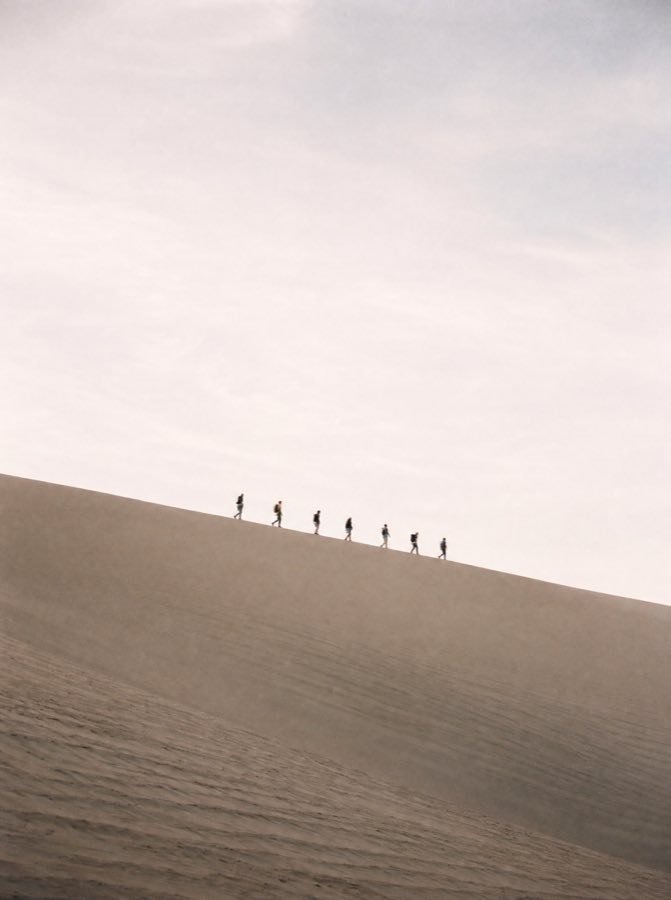 Figuras diminutas en fila india sobre la cresta de una duna.