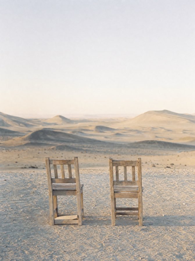 Dos sillas de madera vacías frente a un mar de dunas.