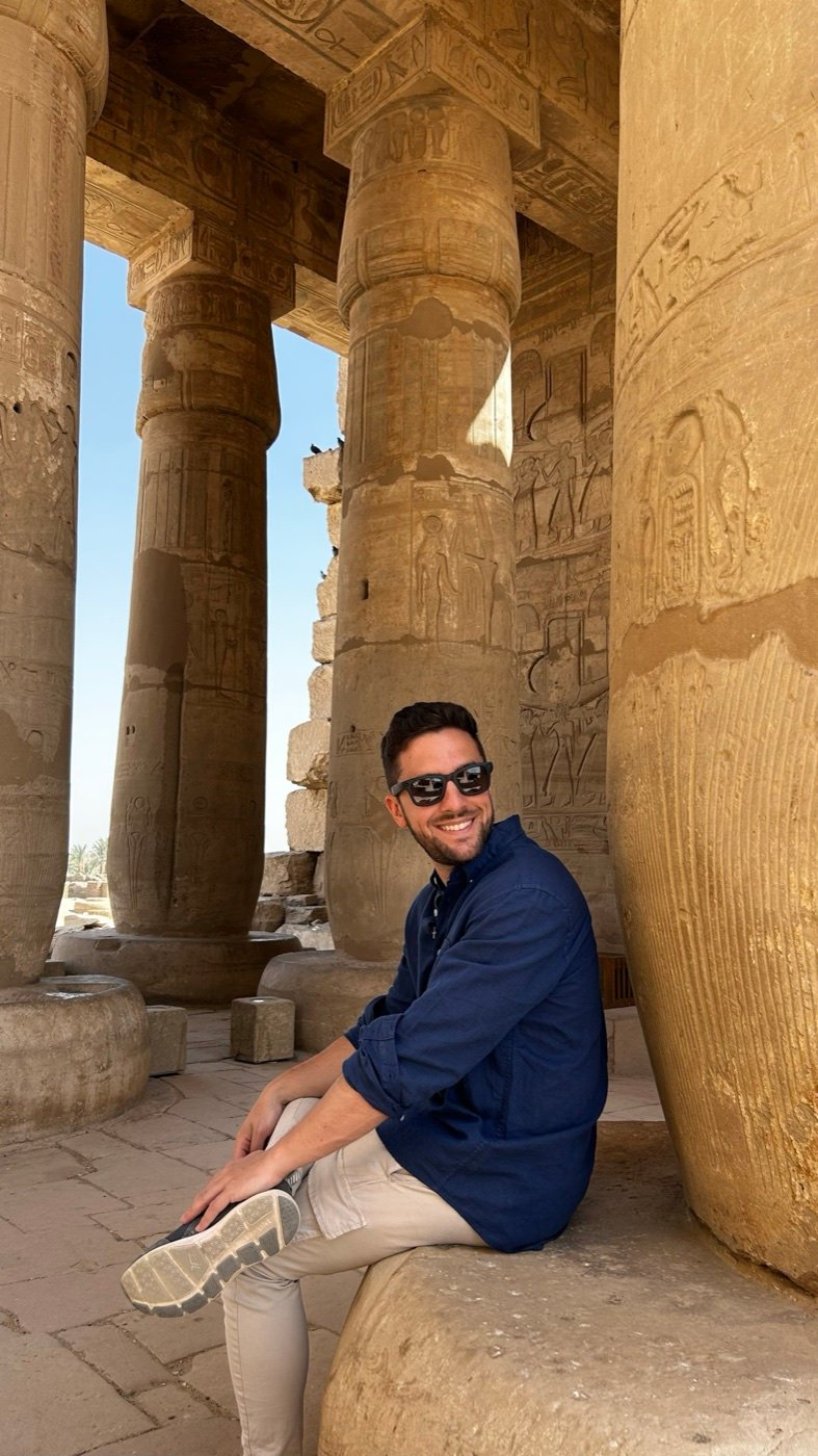 Rubén sentado a la sombra de unas columnas, sonriendo.