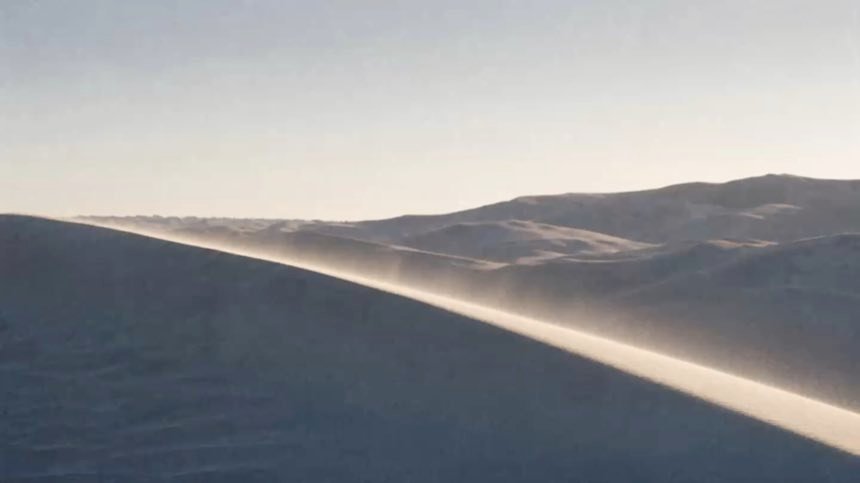 Velo de arena levantándose de la cresta de una duna a contraluz.