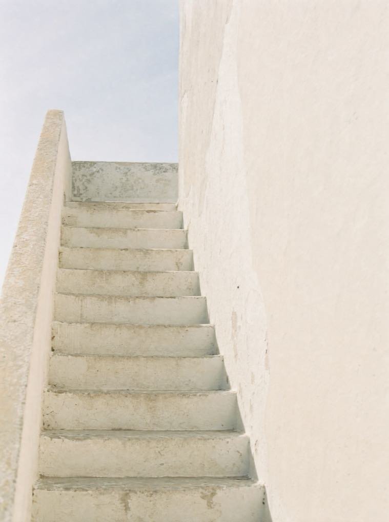 Escalera encalada subiendo a una terraza, con la luz de la mañana entrando de lado.