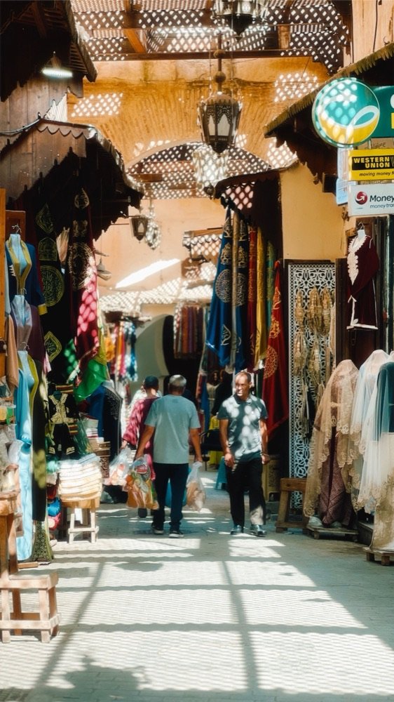 Un callejón del zoco de Marrakech, con puestos de telas y lámparas a los dos lados.